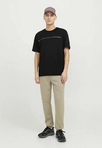 Mustad lühikeste varrukatega t-särk peene horisontaalse triibuga. Beežid kitsenevad püksid õmbluste detailidega. Mustad tossud ja helelilla müts.