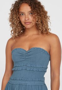 Trägerloses, blaues Kleid aus strukturiertem Stoff mit Rüschendetails und gerafftem Oberteil. Es hat einen taillierten Oberteil und einen ausgestellten Rock.