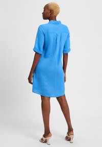 Hellblaues Leinenhemdkleid mit kurzen Ärmeln, Rückenpasse und abgerundetem Saum. Kombiniert mit beigen High-Heel-Sandalen.