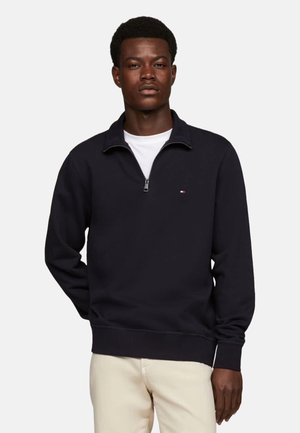 Sudadera navy de media cremallera con cuello y puños acanalados, que presenta un pequeño logo en el pecho. Textura suave, ajuste casual.