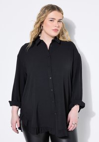 Camisa negra de botón con cuello, que presenta mangas largas, un dobladillo con volantes y un corte relajado. Textura de tela suave.
