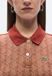 Piros mintás galléros póló, három gombbal és zöld hímzett krokodil logóval a mellkason. Simogató tapintású anyag.