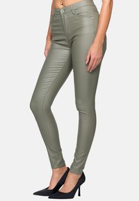 Olivgrön faux läder skinnybyxor med framseams, hög midja och slim fit-design, tillsammans med svarta spetsiga högklackade skor.