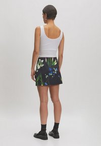 Zwarte rok met kleurrijke bloemenprint, gecombineerd met een witte tanktop. Het ontwerp heeft levendige bloemen en een getailleerde vorm. Zwarte schoenen maken de look compleet.