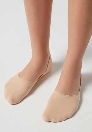 Calcetines bajos de color beige con textura acanalada y punta redondeada, diseñados para cubrir solo el pie, con un acabado suave.
