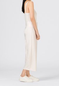 Ljust färgad, ribbad linne med tunna axelband, parat med släta byxor i ankellång längd i ett mjukt, glänsande tyg. Bärs med vita sneakers.