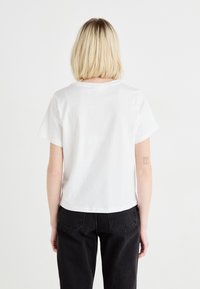 T-shirt en coton blanc à manches courtes, avec un col rond et une coupe décontractée, associé à un jean en denim noir, vu de dos.