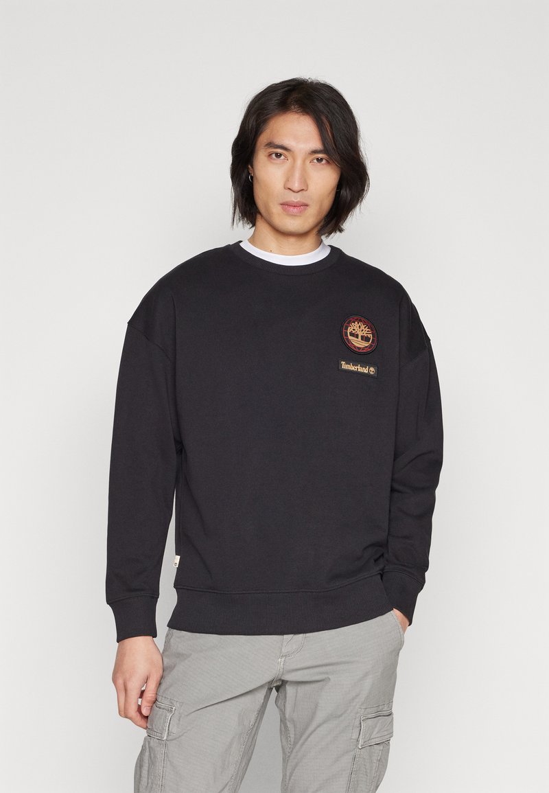 Černé crewneck mikina s žebrovanými manžetami a lemem, se znakem na hrudi. Vyrobena z měkkého materiálu, s volným střihem.
