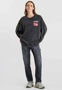 Sweat-shirt noir surdimensionné avec un graphisme de cerises colorées, associé à un jean en denim foncé. Les chaussures présentent des accents gris et argentés.