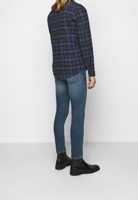 Rutigt skjorta i blått och svart med långa ärmar, kombinerad med tajta blå jeans och svarta ankelstövlar, sedd bakifrån.