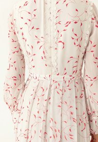 Vestido de tela blanca con delicados patrones de hojas rojas, mangas largas, ribete de encaje a lo largo de la espalda y el escote, y diseño con pliegues en la cintura.