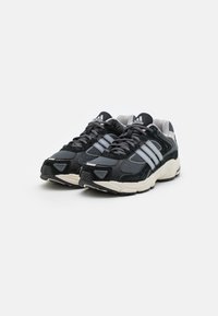 Svart och gråa träningsskor med ovandel i mesh och detaljer i mocka, med tre vita ränder, tjock sula och strukturerat mönster.