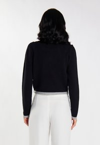 Pulover scurt negru cu mâneci lungi, având o margine vagă gri. Textura pare moale și tricotată, purtat peste pantaloni albi.