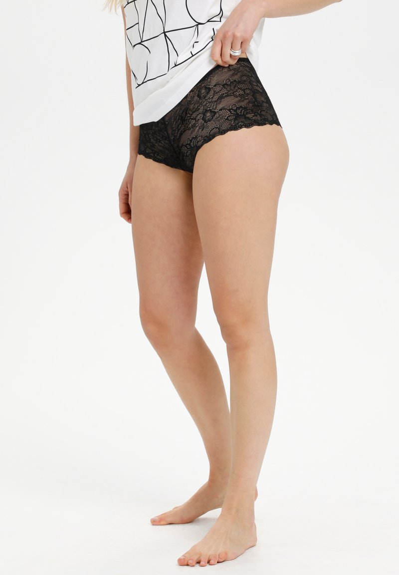 Chiloți hipster din dantelă neagră, cu modele florale, margini ondulate și o textură moale, transparentă. Asortați cu un top alb lejer.
