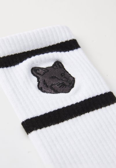 Chaussette blanche à crew avec des rayures noires horizontales et un visage d'animal brodé noir sur le côté ; texture côtelée sur toute la surface.