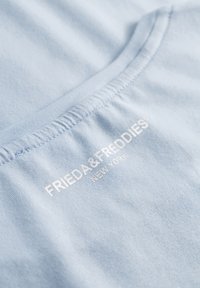 Lichtblauw katoenen t-shirt met een klassieke ronde hals en een geborduurd etiket met de tekst "FRIEDA & FREDDIES NEW YORK" in het wit.