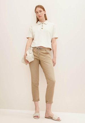 Afgesneden witte polo-shirt met drie bruine knopen, gecombineerd met beige opgerolde broek en lichtbeige slippertjes. Inclusief een klein wit handtasje.