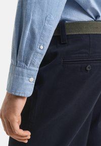 Lichtblauwe overhemdd met een gestructureerde kraag en manchetten, gecombineerd met donkerblauwe broek met een riem met een gematteerde afwerking.