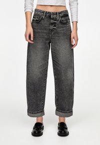 Jean en denim noir taille haute avec une coupe décontractée, cinq poches, revers retroussés, présentant un lavage délavé et des détails de coutures visibles.