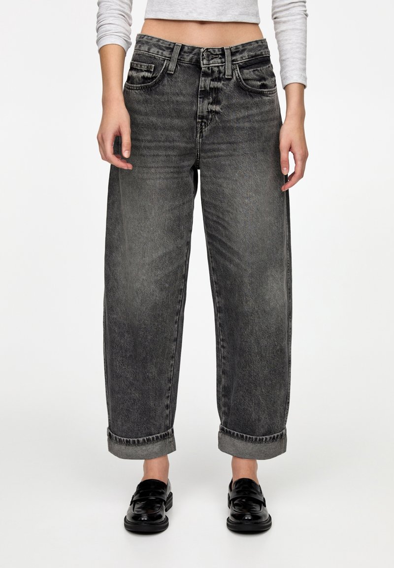 Jean en denim noir taille haute avec une coupe décontractée, cinq poches, revers retroussés, présentant un lavage délavé et des détails de coutures visibles.