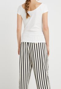 Biała bluzka z krótkim rękawem i zaokrąglonym dekoltem z tyłu, w połączeniu z szerokimi spodniami w czarno-białe paski z guzikami.