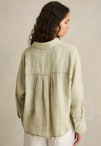 Hellgrünes Leinenhemd mit lockerer Passform, Rückenfalten und geknöpften Manschetten. Verfügt über einen klassischen Kragen und glattes, leicht strukturiertes Material.