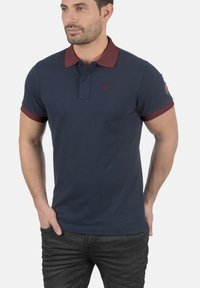 Marineblå polo-shirt lavet af bomuld, med en bordeaux farvet krave og ærmekant, knaplukning og et lille logo på brystet.