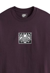 Luźny, ciemnofioletowy t-shirt z grafiką przedstawiającą twarz z wyeksponowanymi zębami oraz napisem „VANS OFF THE WALL” w czerni i bieli.