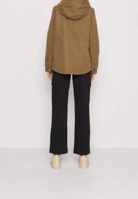 Brun huva jacka gjord av mjukt tyg, kombinerad med lösa svarta byxor. Outfiten har en minimal design utan synliga mönster eller detaljer.