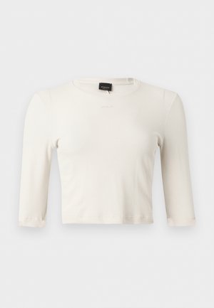 Balta sieviešu cropped topiņa ar riboto adījumu, garām piedurknēm, apaļu kakla izgriezumu un sīku izšūtu zīmola logotipu krūtīs.