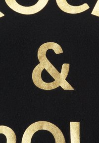 Tessuto nero con grande testo dorato lucido che presenta un simbolo di e commerciale e lettere solide adiacenti, creando un contrasto grafico audace.