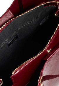 Sac à main structuré en cuir bordeaux, doté d'une poche zippée, de quincaillerie dorée et d'un intérieur en tissu noir avec plusieurs compartiments.