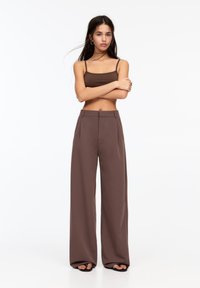 Hnědé široké kalhoty, lehká tkanina, sklady vpředu, vysoký pas, spárované s odpovídajícím hnědým crop topem. Hladká textura, minimalistický design.
