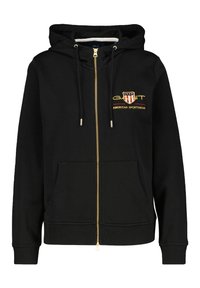 Zwarte rits hoodie van zacht materiaal, met een gouden rits, voorzakken en een geborduurd logo met rode en witte accenten.