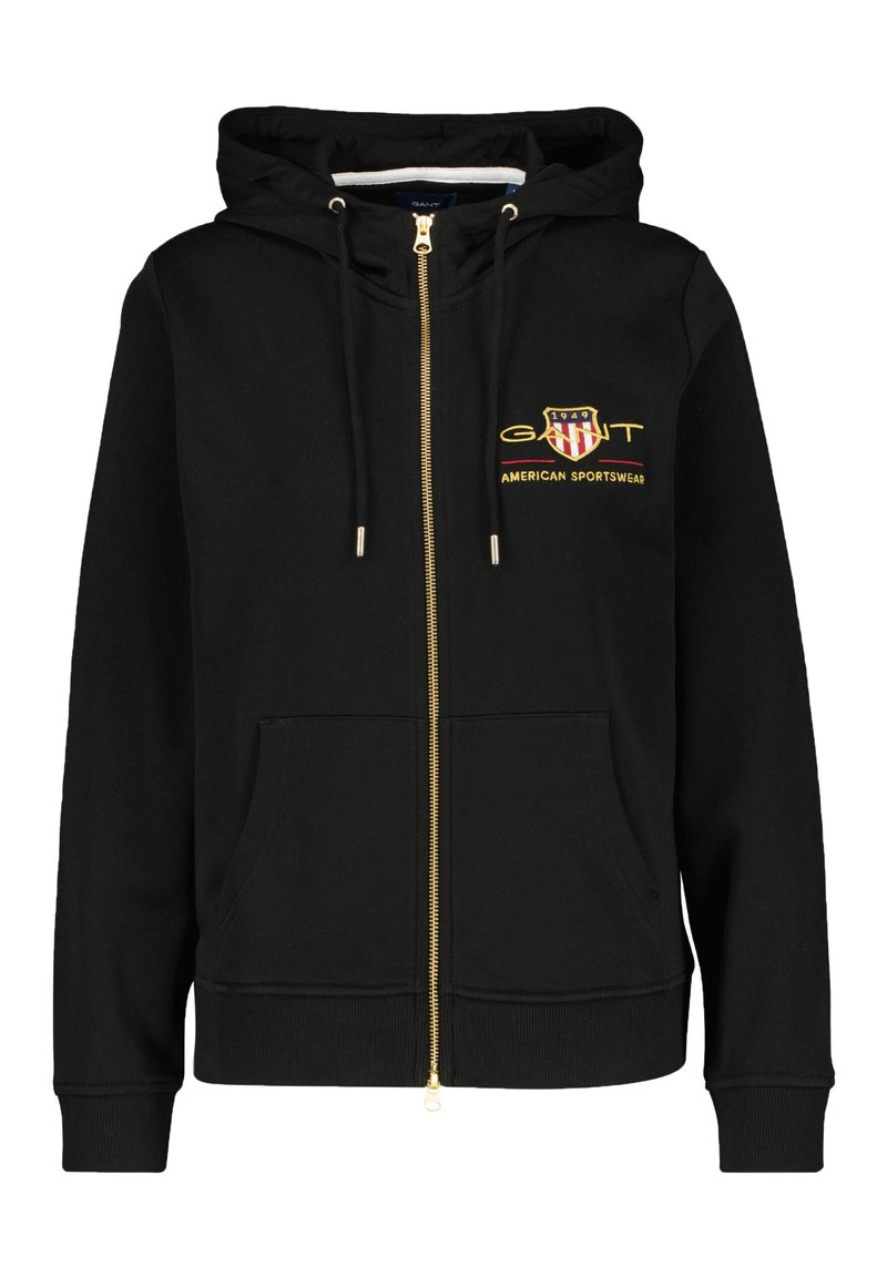 Zwarte rits hoodie van zacht materiaal, met een gouden rits, voorzakken en een geborduurd logo met rode en witte accenten.