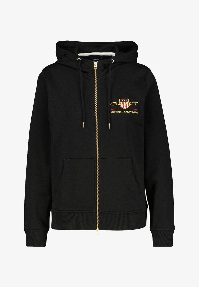 Zwarte rits hoodie van zacht materiaal, met een gouden rits, voorzakken en een geborduurd logo met rode en witte accenten.