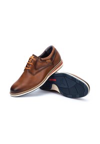 Zapatos de vestir de cuero marrón con puntera redondeada, costuras en contraste, cordones y una suela media blanca. Suela de goma negra con relieve y detalle del logo.