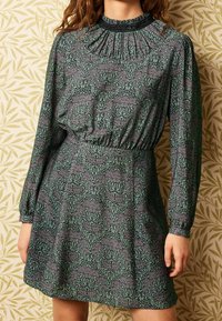 Vestido de manga larga en tejido verde oscuro con un estampado floral. Escote fruncido con cintura elástica y puños con voluminosos.