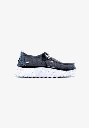 Zapatos gris tipo slip-on con un respaldo texturizado, que cuentan con una suela blanca salpicada y cordones elásticos para facilitar su colocación. Parte superior de tela suave.
