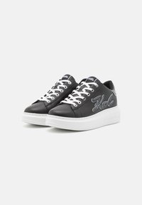 Zapatillas de piel negra con suela y cordones blancos. Presentan un logotipo bordado de "Karl" en blanco en el lateral. Diseño de puntera redondeada.