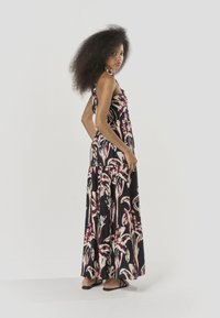 Vestido maxi de tela negra con un estampado floral en crema y rojo. Presenta un corpiño ceñido y una falda fluida. Las sandalias acentúan el look.