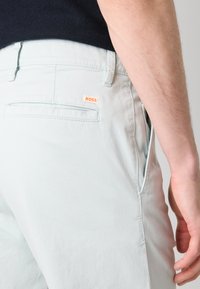 Pantaloni bleu deschis cu croi slim, având un buzunar la spate și un label mic portocaliu "BOSS". Realizați dintr-un material moale și neted.