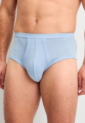 Man die lichtblauwe katoenen slips draagt, staand tegen een effen achtergrond, getoond van taille tot halverwege het dijbeen.