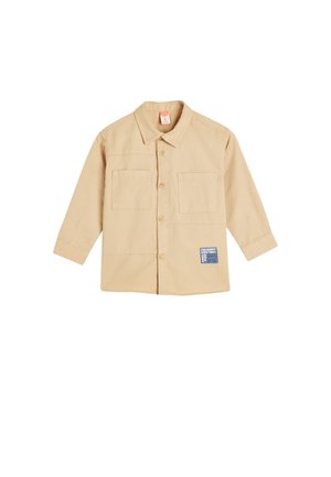 Beige Hemd mit langen Ärmeln, zwei Brusttaschen und einem Etikett auf der linken Unterseite. Hergestellt aus Baumwollstoff mit glatter Textur.