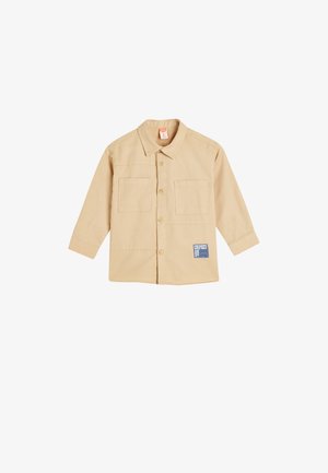 Camisa beige de botones con mangas largas, dos bolsillos en el pecho y una etiqueta en el lado inferior izquierdo. Fabricada en tela de algodón con una textura suave.