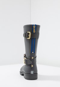 Bota de goma gris con un cierre azul, acentos de hebilla dorada y una suela texturizada. El diseño incluye una pantorrilla ancha y una construcción resistente.