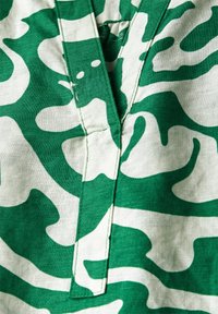 Tela verde y blanca con un diseño de camuflaje, con un acabado texturizado y una abertura vertical en el escote.