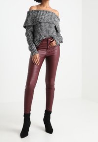 Jersey gris de punto con escote al descubierto y textura acanalada, combinado con pantalones pitillo de cuero sintético burdeos y botines negros.