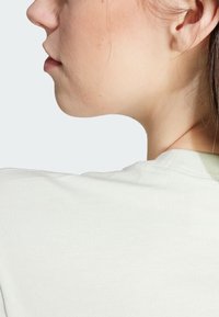 Camiseta gris claro con una textura suave, escote redondo y costuras visibles. La tela parece ligeramente elástica y ligera.