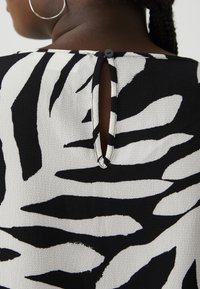 Black and white patterned fabric featuring leaf-like designs, with a button closure at the back and a keyhole detail. Textured surface.
